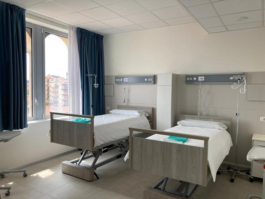 Camera di degenza doppia moderna, con letti elettrici regolabili, finestre ampie, tende oscuranti e attrezzature mediche a parete