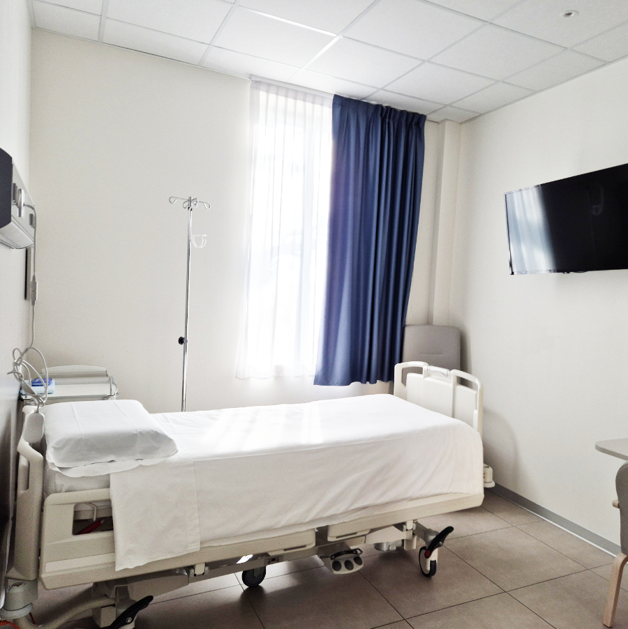 Clinica Isber - Degenza. Camera di degenza ospedaliera moderna con letto regolabile, TV a parete, finestra con tenda e arredi essenziali in un ambiente pulito e luminoso.